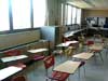 Two rows of student desks in front of some windows and a line of computers in the back.